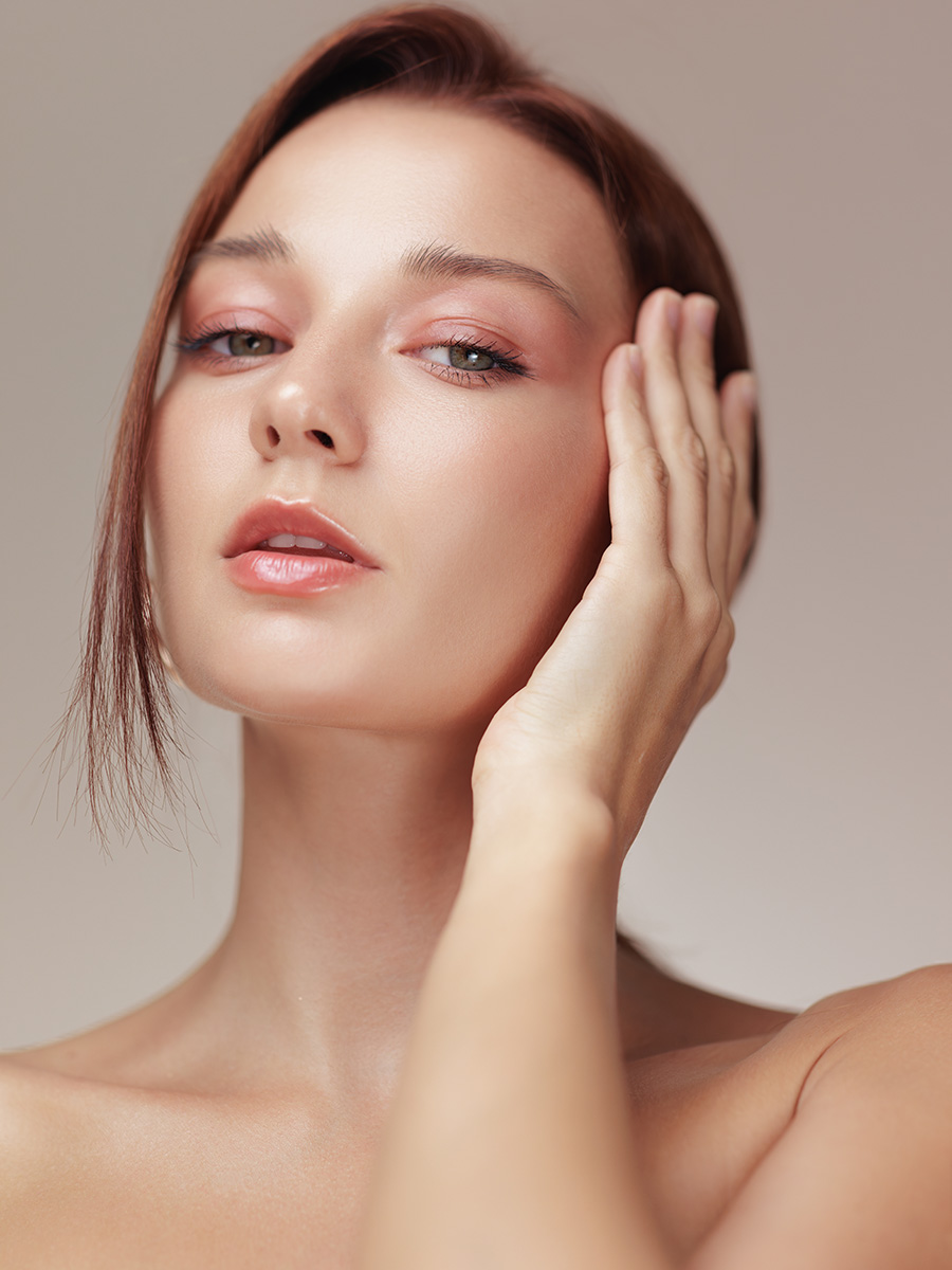 Young woman with glowing skin touching her face